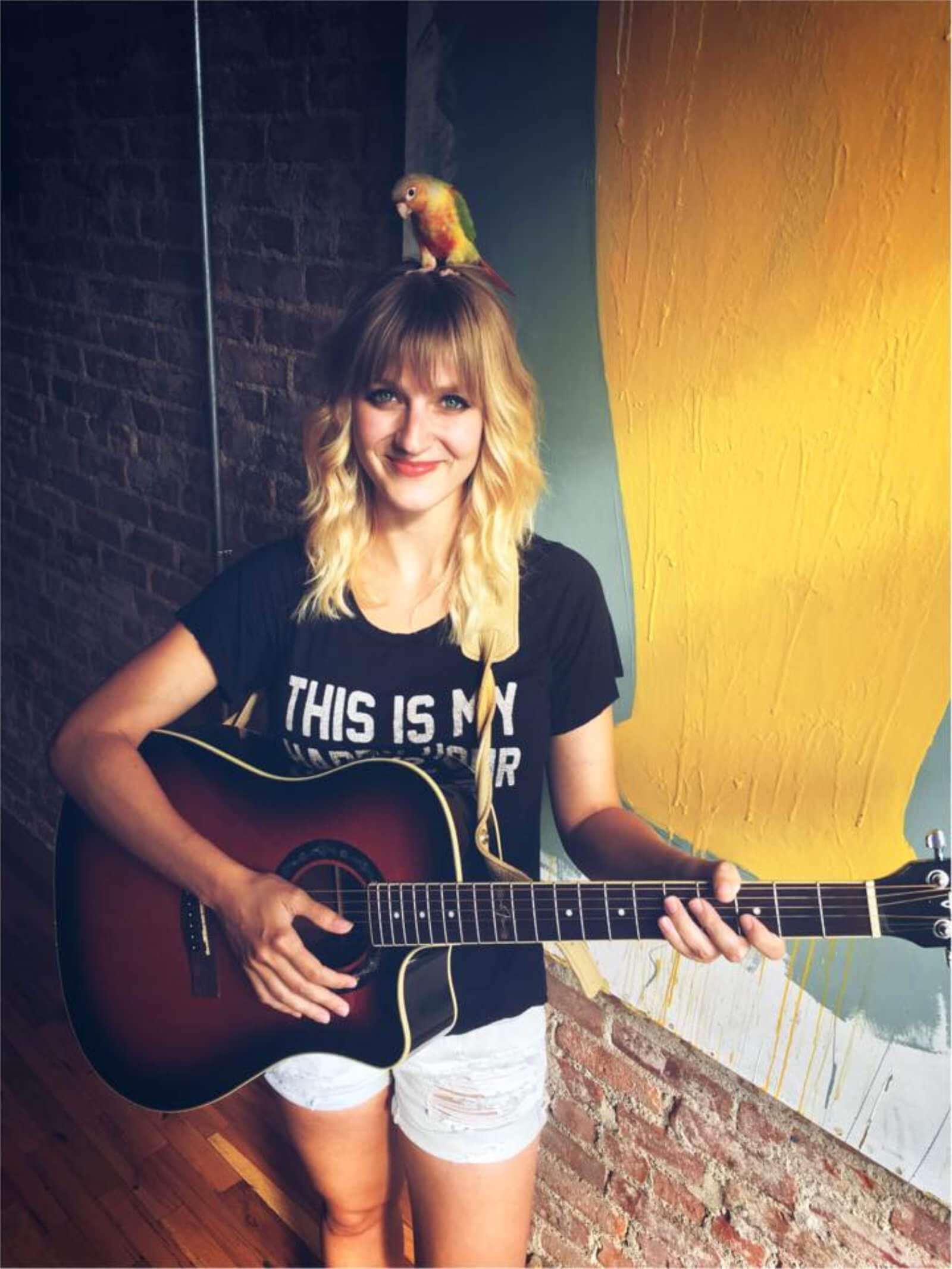 Julia Green with a guitar and a bird on her head